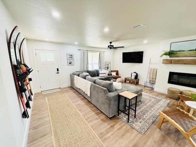 living room featuring ceiling fan, a textured ceiling, and light hardwood / wood-style floors