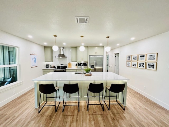 kitchen featuring wall chimney exhaust hood, a spacious island, appliances with stainless steel finishes, and hanging light fixtures