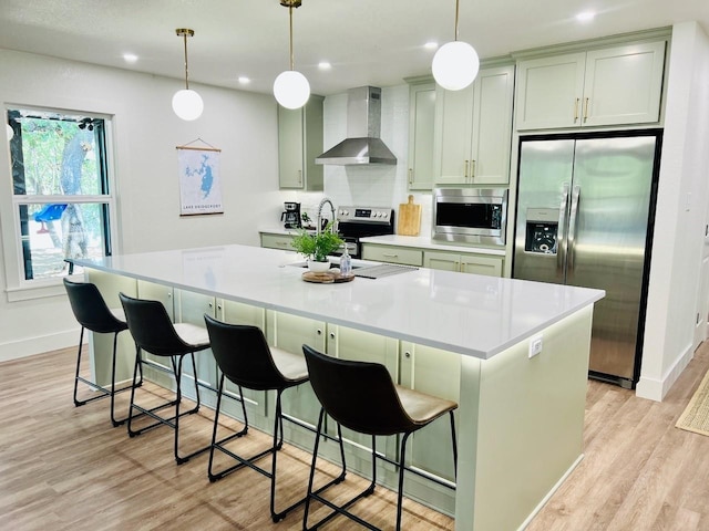 kitchen with wall chimney exhaust hood, stainless steel appliances, a breakfast bar, and a center island with sink