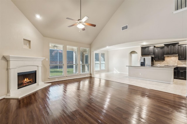 unfurnished living room with high vaulted ceiling, light wood-type flooring, and ceiling fan