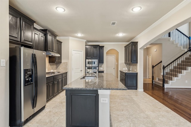 kitchen with sink, crown molding, appliances with stainless steel finishes, tasteful backsplash, and an island with sink