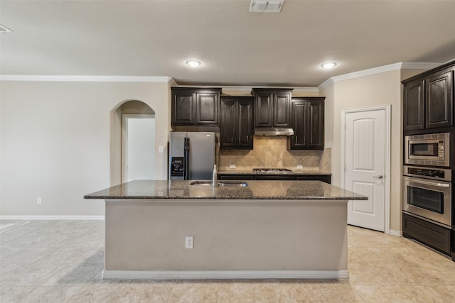 kitchen with tasteful backsplash, appliances with stainless steel finishes, an island with sink, and dark stone countertops