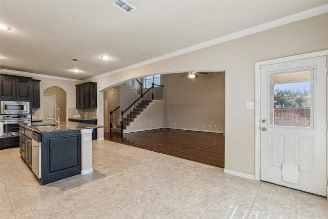 kitchen with appliances with stainless steel finishes, sink, backsplash, dark brown cabinetry, and a center island with sink