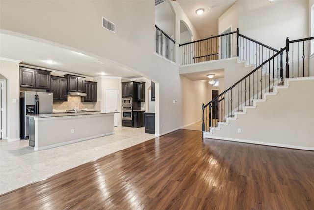 unfurnished living room with sink, light hardwood / wood-style flooring, ornamental molding, and a high ceiling