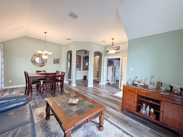 living room with hardwood / wood-style flooring, an inviting chandelier, and vaulted ceiling