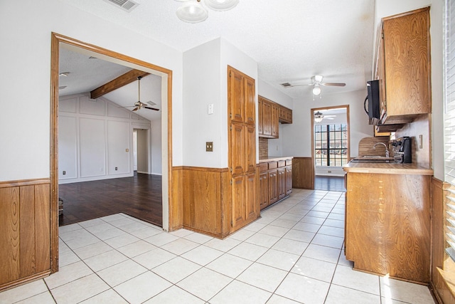 kitchen featuring brown cabinetry, light tile patterned flooring, light countertops, and wainscoting