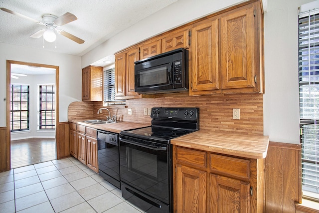 kitchen featuring brown cabinets, light tile patterned floors, light countertops, a sink, and black appliances