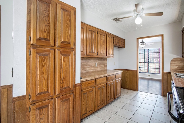 kitchen featuring light tile patterned floors, a wainscoted wall, visible vents, light countertops, and brown cabinetry