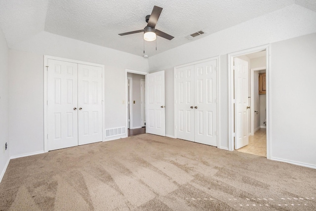 unfurnished bedroom with light colored carpet, visible vents, a textured ceiling, and two closets