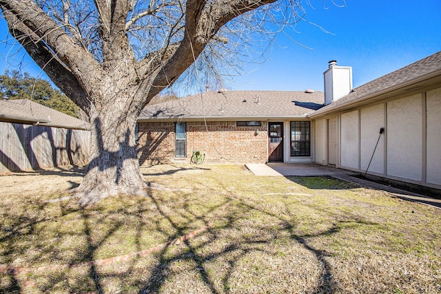 back of property featuring a chimney, roof with shingles, fence, a yard, and brick siding