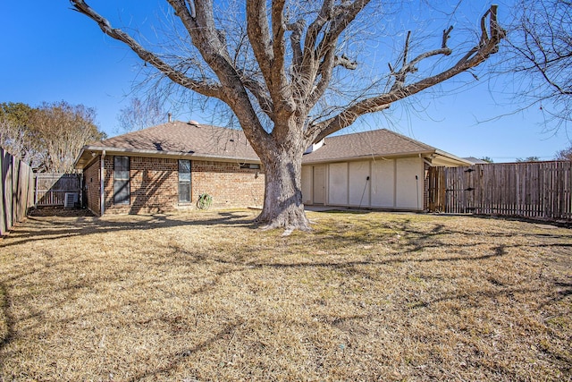 rear view of property with a yard, a fenced backyard, a shingled roof, and brick siding