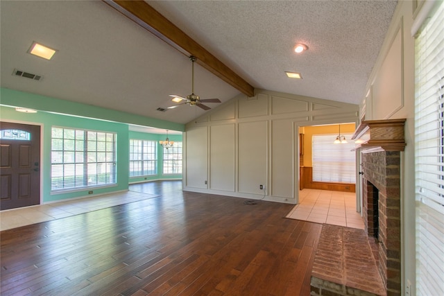 unfurnished living room with ceiling fan with notable chandelier, a fireplace, vaulted ceiling with beams, a textured ceiling, and light hardwood / wood-style flooring