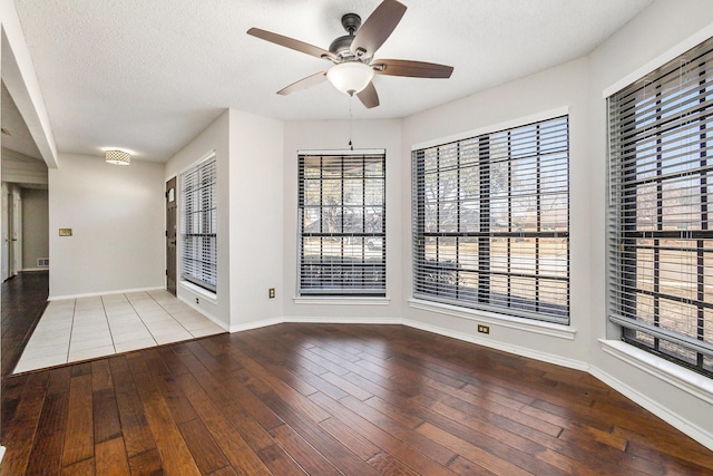 spare room with a textured ceiling, ceiling fan, light wood-type flooring, and baseboards