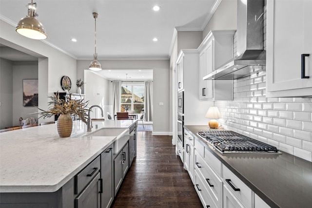 kitchen with dark wood finished floors, a sink, appliances with stainless steel finishes, wall chimney range hood, and tasteful backsplash