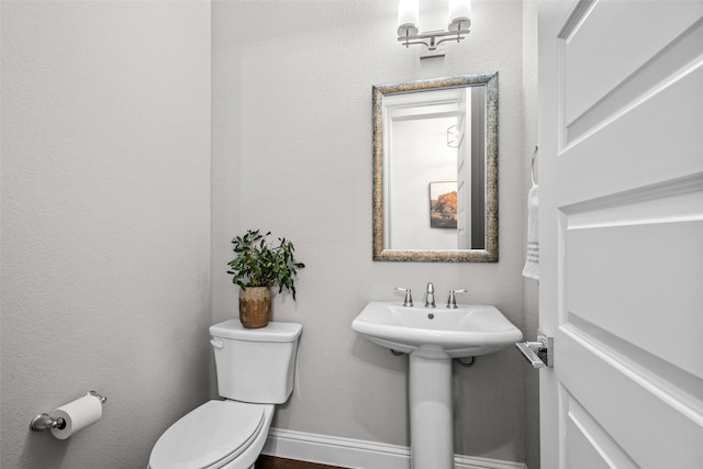 half bath featuring toilet, baseboards, and a sink