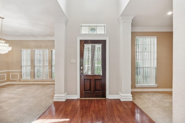 foyer entrance with ornamental molding, decorative columns, carpet, and a notable chandelier