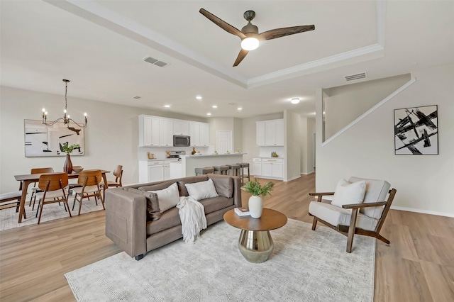 living room featuring crown molding, ceiling fan with notable chandelier, light hardwood / wood-style flooring, and a raised ceiling