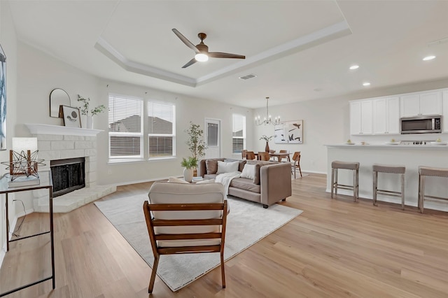 living room featuring a tray ceiling, light hardwood / wood-style flooring, and ceiling fan with notable chandelier