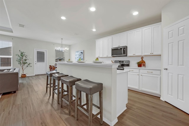 kitchen featuring stainless steel appliances, white cabinetry, pendant lighting, and a center island with sink