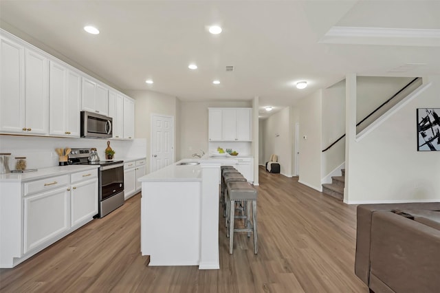 kitchen featuring appliances with stainless steel finishes, white cabinetry, a breakfast bar area, a kitchen island with sink, and light wood-type flooring