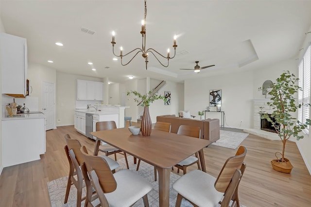 dining space featuring sink, a tray ceiling, light hardwood / wood-style floors, and ceiling fan