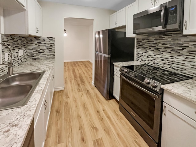 kitchen featuring sink, light stone counters, light hardwood / wood-style flooring, appliances with stainless steel finishes, and white cabinets