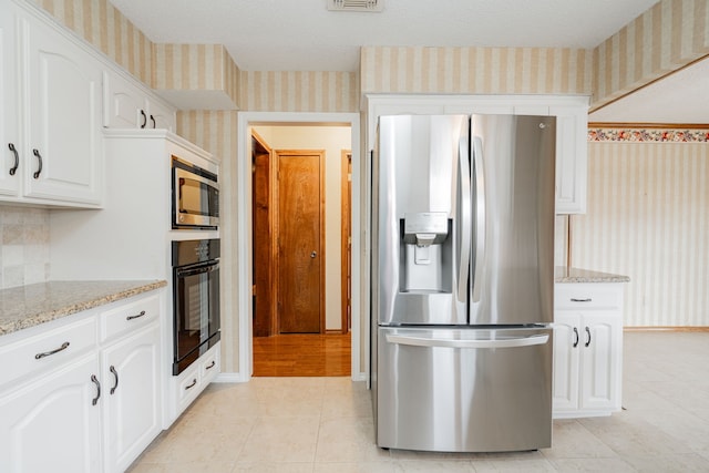 kitchen featuring light tile patterned flooring, white cabinetry, a textured ceiling, stainless steel appliances, and light stone countertops