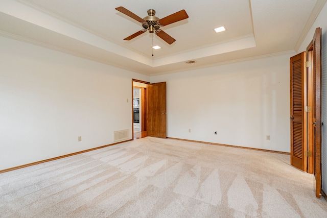 unfurnished bedroom with ornamental molding, light carpet, ceiling fan, and a tray ceiling