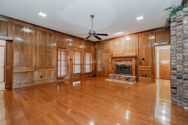 unfurnished living room featuring a brick fireplace, light hardwood / wood-style floors, ceiling fan, and wood walls