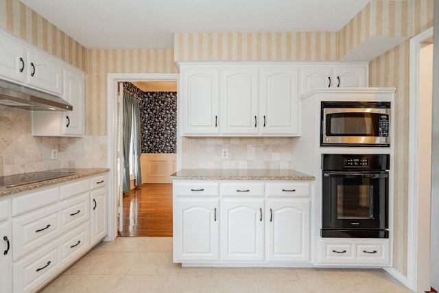 kitchen featuring light tile patterned flooring, light stone countertops, white cabinets, and black appliances