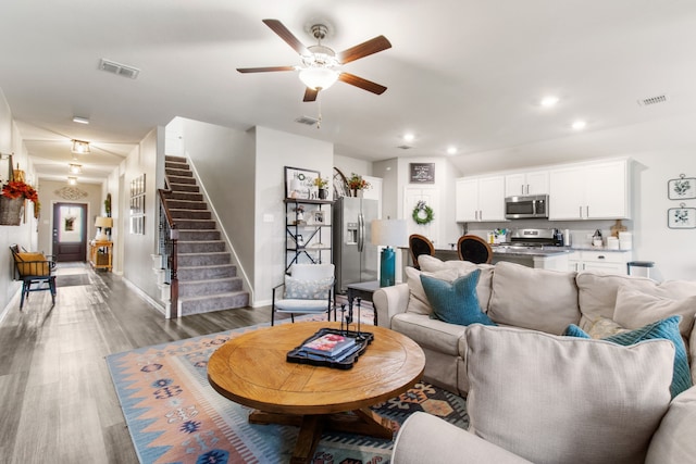 living room featuring ceiling fan, visible vents, wood finished floors, and stairs