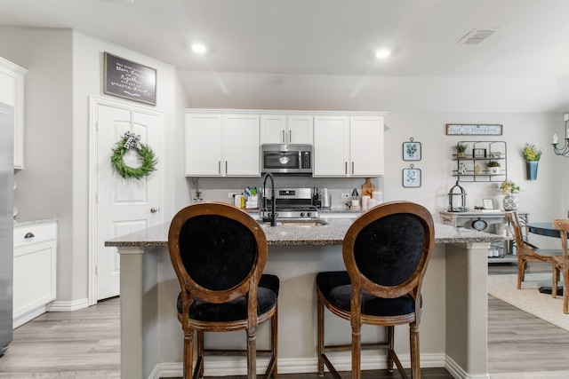 kitchen featuring white cabinetry, light stone counters, a kitchen island with sink, and stainless steel appliances