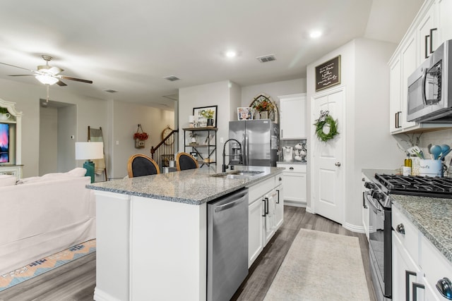 kitchen with appliances with stainless steel finishes, white cabinetry, light stone counters, dark wood-type flooring, and a center island with sink