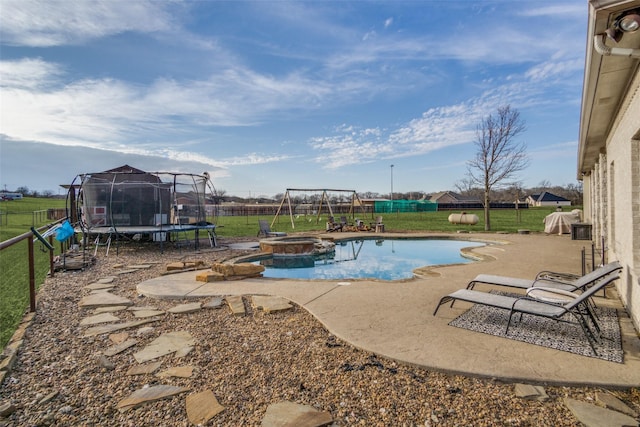 view of pool with an in ground hot tub, a lawn, a trampoline, and a patio area