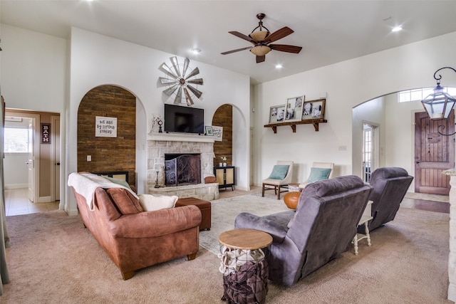 carpeted living room with a stone fireplace, ceiling fan, and a towering ceiling