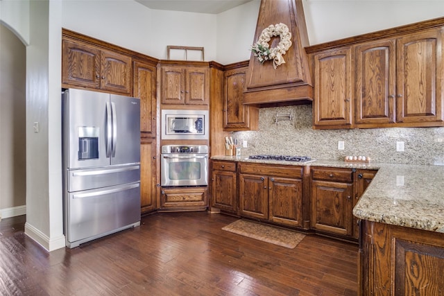 kitchen with premium range hood, tasteful backsplash, appliances with stainless steel finishes, dark hardwood / wood-style flooring, and light stone countertops