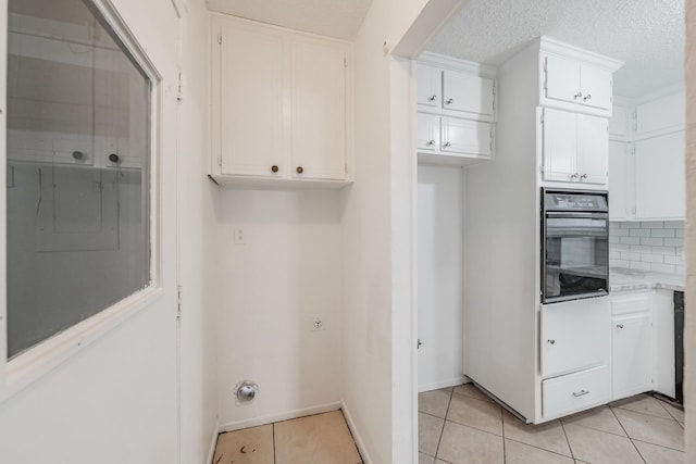 kitchen with white cabinets, light tile patterned floors, oven, and backsplash