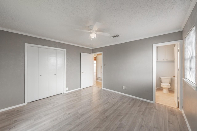 unfurnished bedroom featuring ensuite bathroom, ornamental molding, a textured ceiling, a closet, and light wood-type flooring