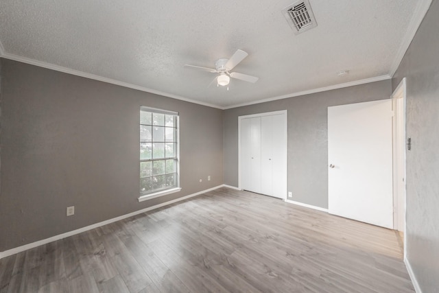 unfurnished bedroom with a textured ceiling, ornamental molding, a closet, ceiling fan, and light hardwood / wood-style floors