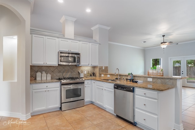 kitchen with sink, white cabinetry, stainless steel appliances, light stone countertops, and kitchen peninsula