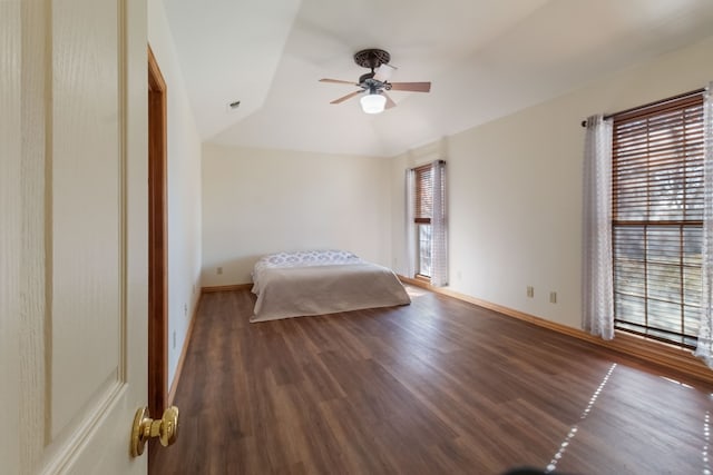 unfurnished bedroom featuring multiple windows, vaulted ceiling, dark wood-type flooring, and ceiling fan