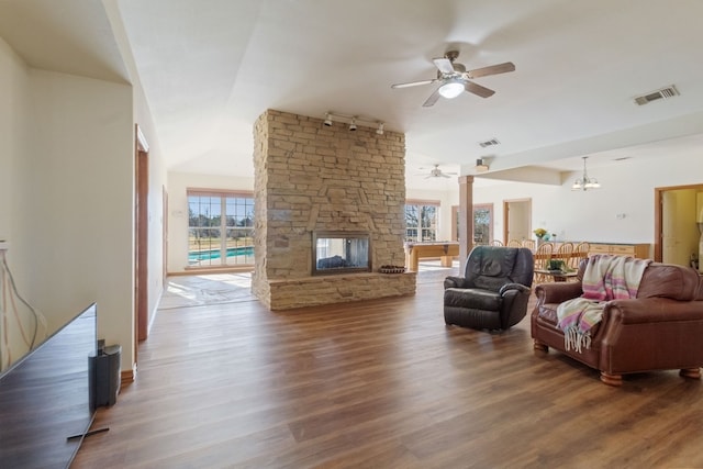 living room featuring a stone fireplace, dark wood-type flooring, ceiling fan with notable chandelier, and lofted ceiling