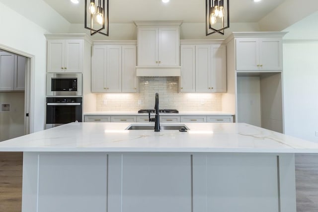 kitchen featuring wall oven, decorative light fixtures, and an island with sink