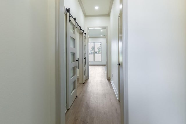 hall with crown molding, a barn door, and light wood-type flooring