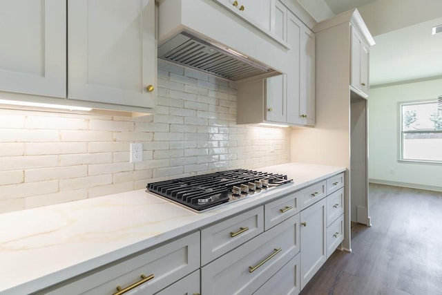 kitchen with backsplash, light stone counters, white cabinets, custom exhaust hood, and stainless steel gas stovetop