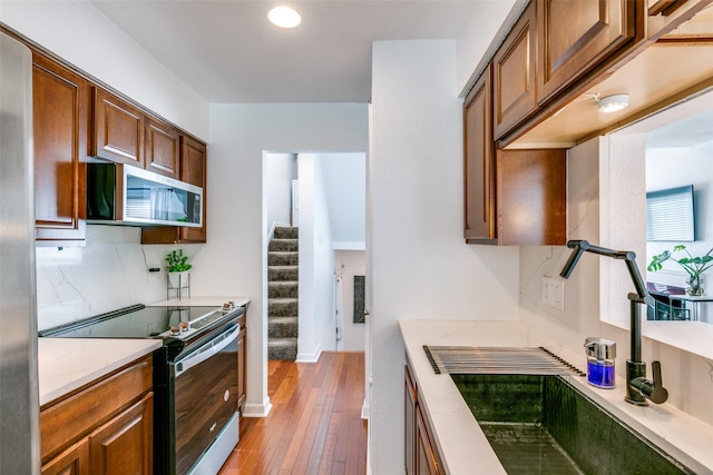 kitchen featuring tasteful backsplash, appliances with stainless steel finishes, light stone countertops, and light hardwood / wood-style floors