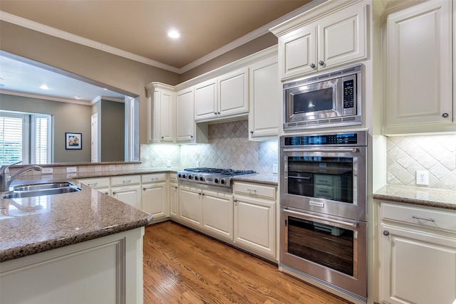 kitchen with sink, white cabinetry, ornamental molding, kitchen peninsula, and stainless steel appliances