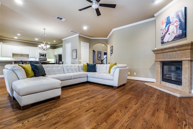 living room featuring crown molding, dark wood-type flooring, a fireplace, and ceiling fan with notable chandelier