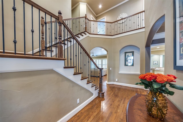 foyer with ornamental molding, wood-type flooring, and a towering ceiling