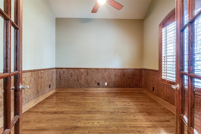 empty room featuring hardwood / wood-style flooring, wood walls, ceiling fan, and a wealth of natural light